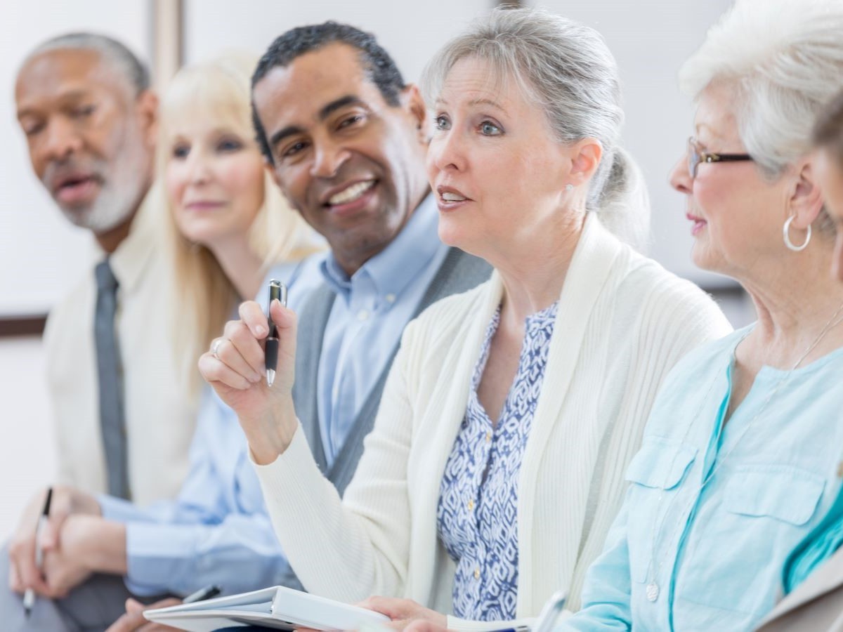 A row of seniors at an event, with one woman asking a question