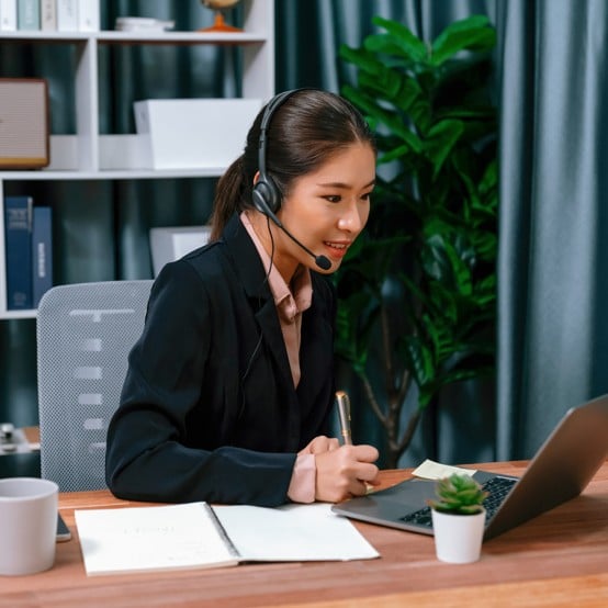 Asian woman with headset watching video conference on laptop